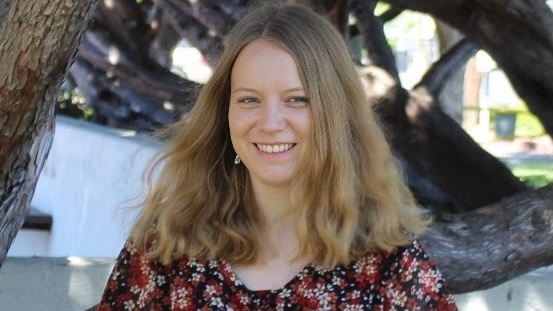 A young woman smiling, standing in front of a tree.