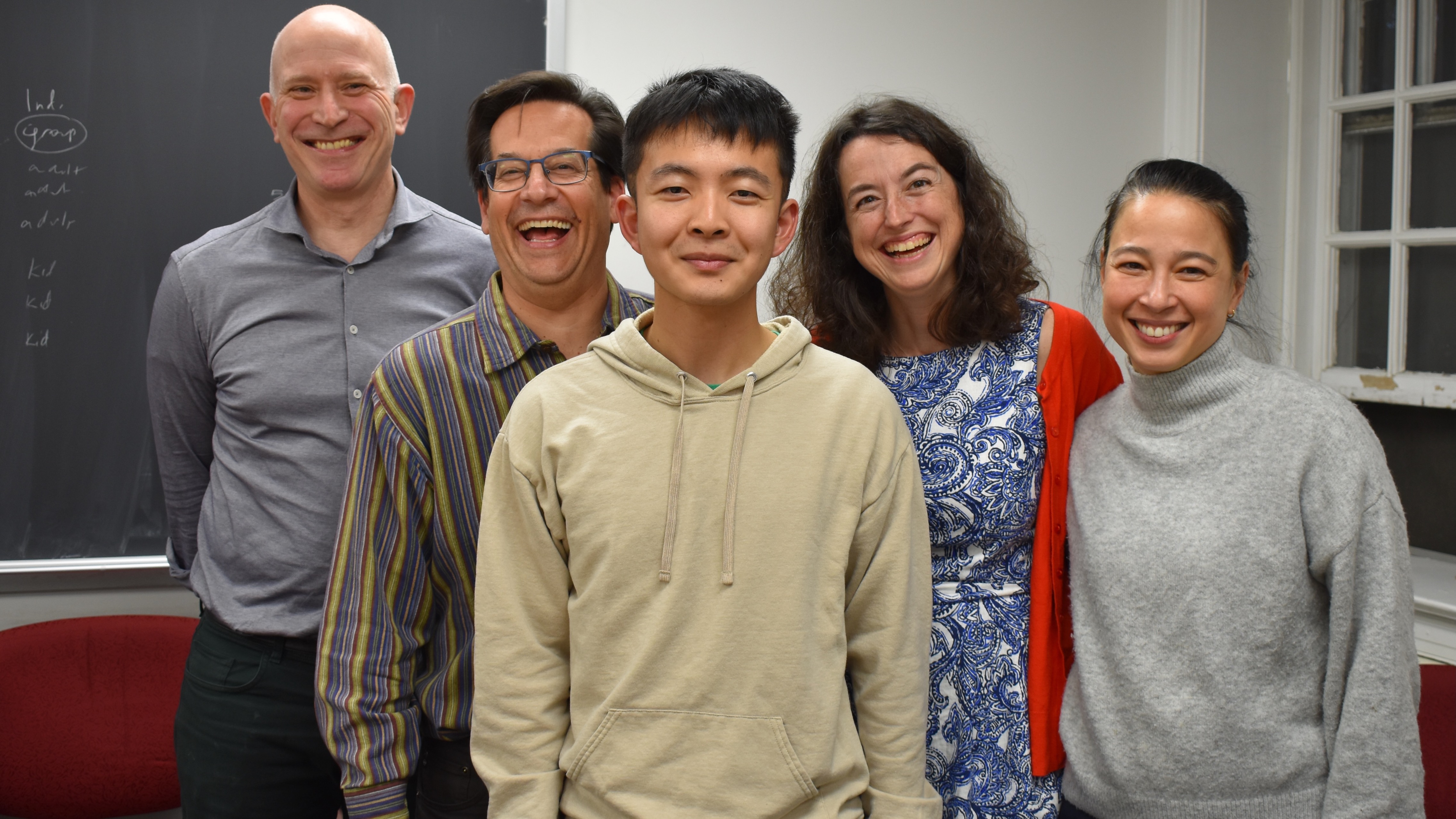 A young man, flanked by the four members of his PhD qualifying committee, two on either side, all of them laughing.